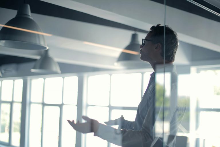 Business professional giving a presentation in a modern office setting through glass.